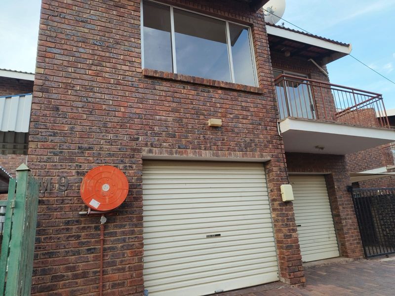 Front exterior view of a face brick apartment building featuring roller shutter garage doors and an upper-level balcony with metal railings.