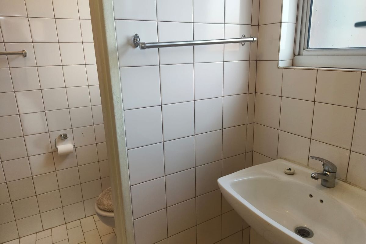 A functional bathroom featuring white wall tiles, a pedestal washbasin with a chrome mixer tap, and a window for natural light.