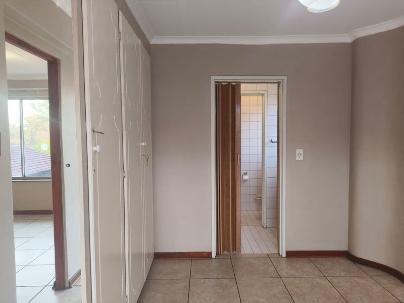 An empty bedroom featuring built-in cupboards, tiled flooring, and a folding door leading to an en-suite bathroom.
