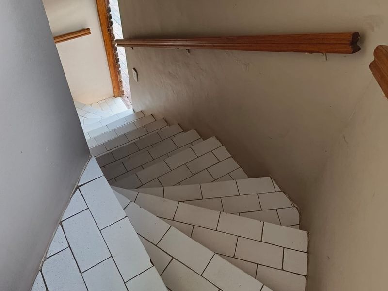 A winding staircase featuring white tiled steps and a wooden handrail, providing access between levels in the apartment.