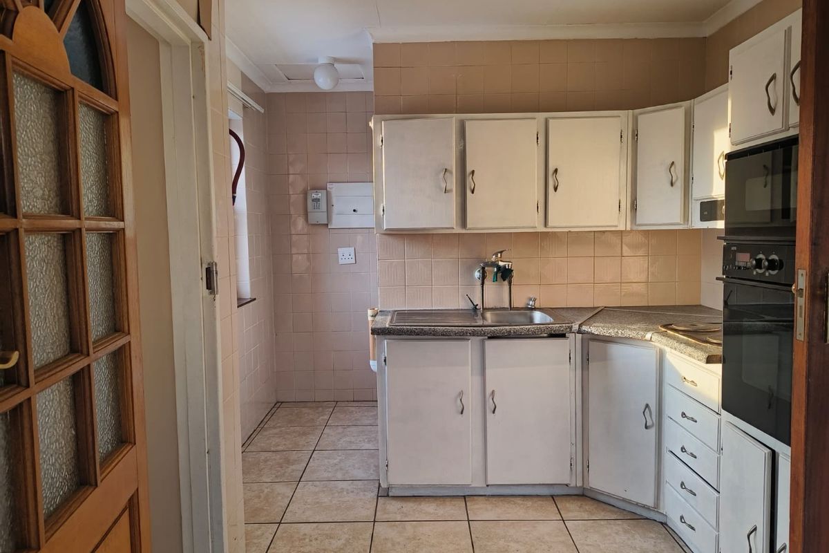 A dated kitchen featuring built-in cabinetry, laminate countertops, a stainless steel sink, and a built-in oven, finished with ceramic wall and floor tiles.