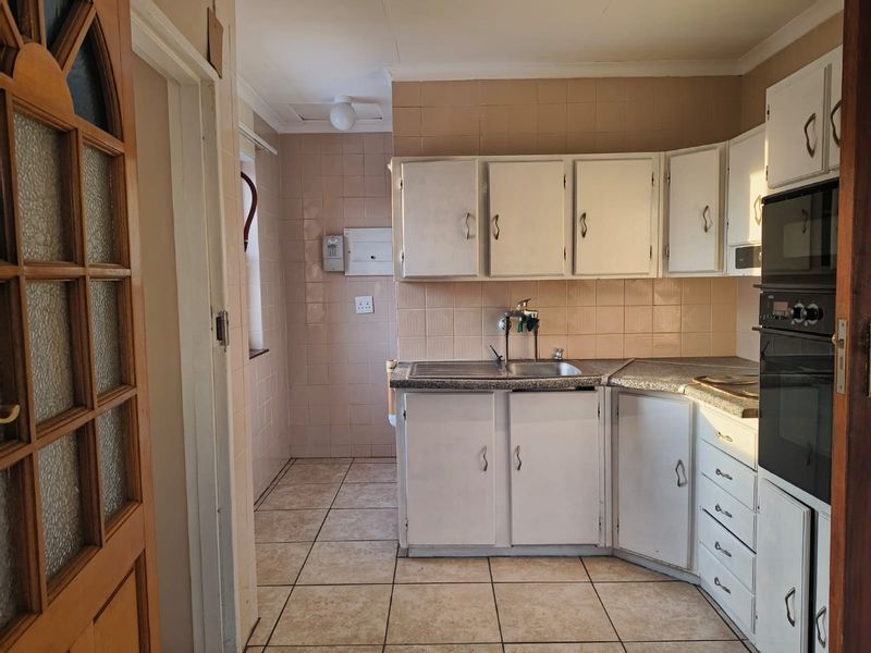 A dated kitchen featuring built-in cabinetry, laminate countertops, a stainless steel sink, and a built-in oven, finished with ceramic wall and floor tiles.