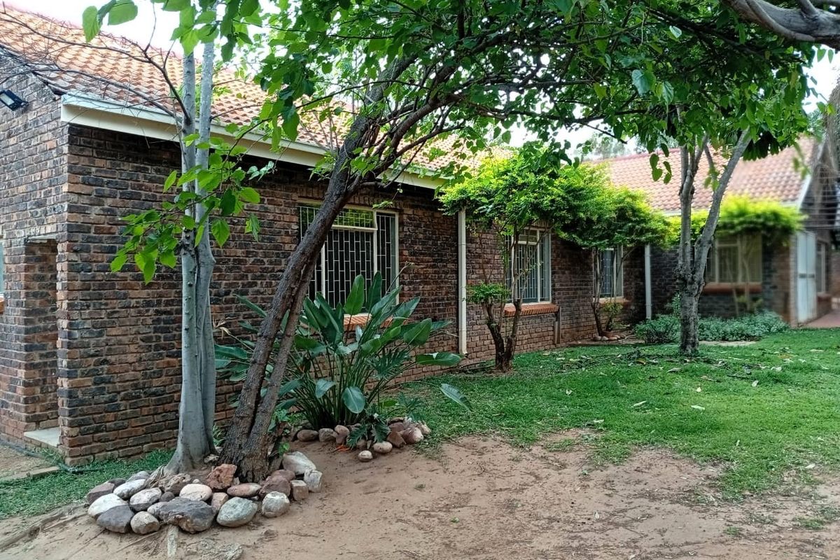 A view of the rear face brick facade of the house, featuring terracotta roof tiles, security-barred windows, and a mature garden setting.