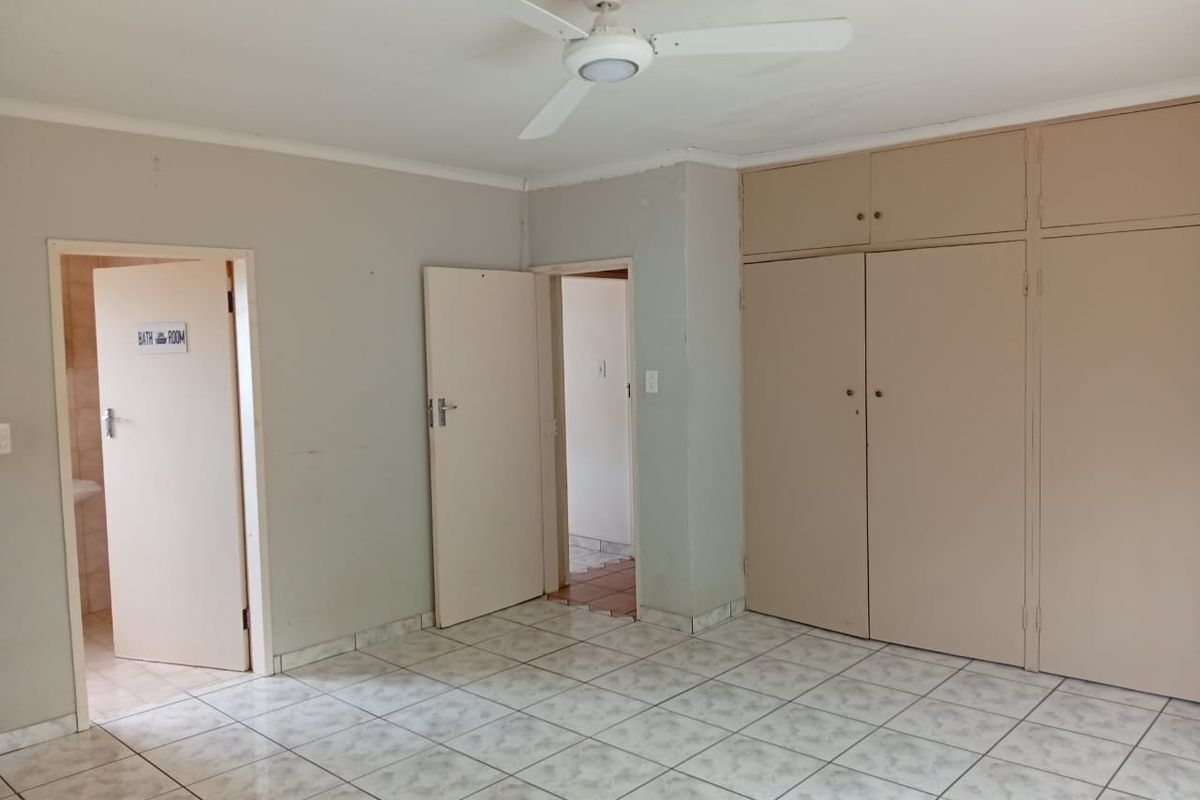 A spacious, empty bedroom featuring tiled flooring, a ceiling fan, and extensive built-in cupboard storage with direct access to an adjacent bathroom.