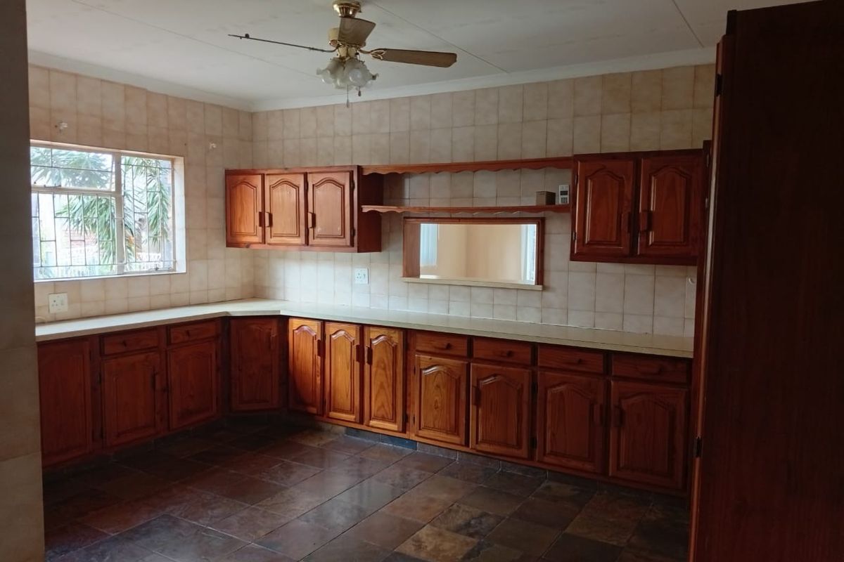 Spacious kitchen featuring traditional wooden cabinetry, tiled splashbacks, and a functional pass-through window, offering a classic layout ready for modern updates.