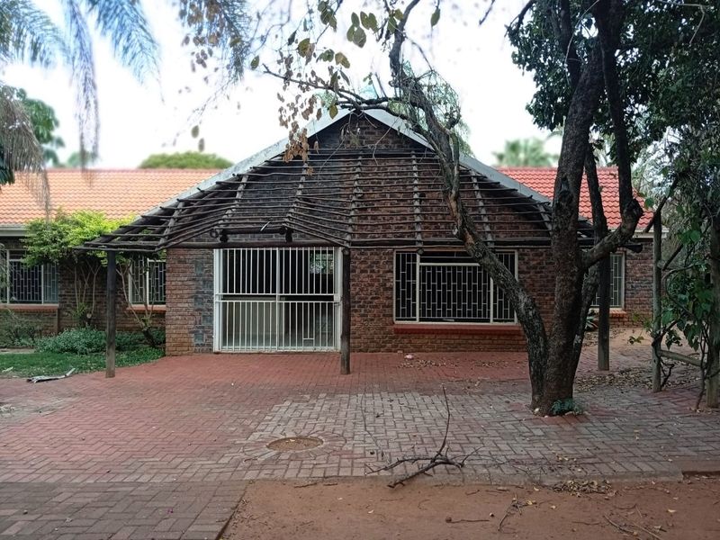 Rear view of a brick house featuring a paved patio area, security bars on windows, and a damaged timber pergola structure.