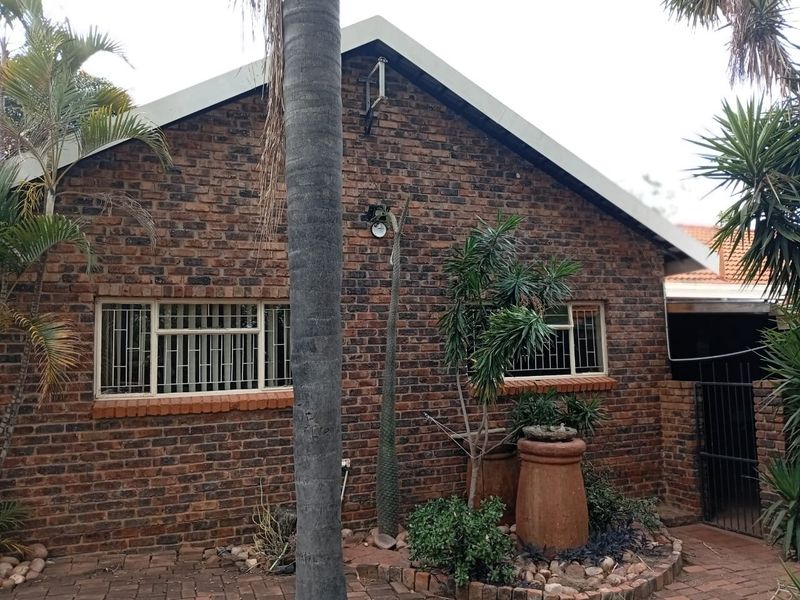 A rear exterior view of a face brick house featuring a gabled roof, security bars on windows, and a paved patio area.