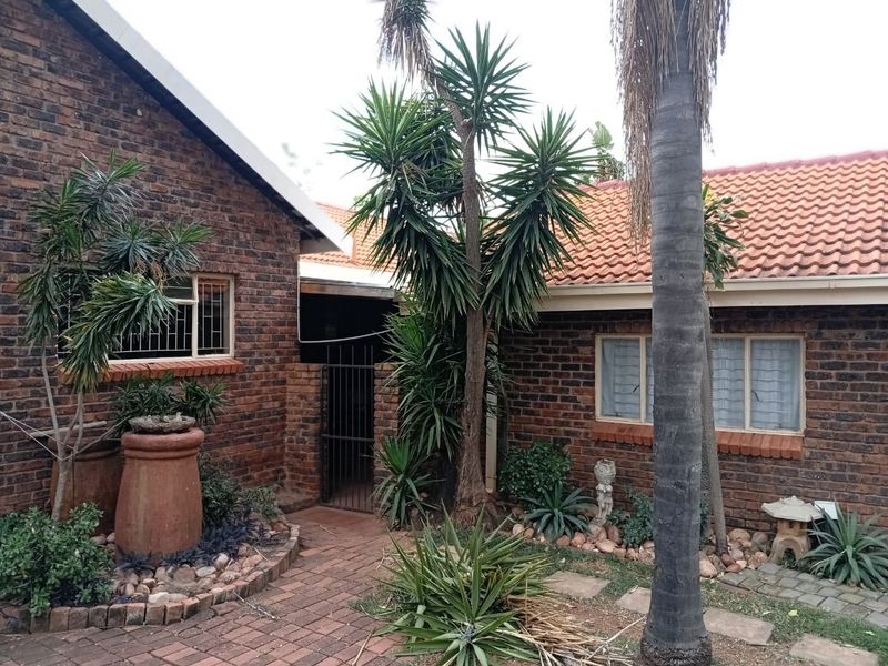 A rear exterior view of a face brick house featuring a tiled roof, security-barred windows, and a paved garden walkway.