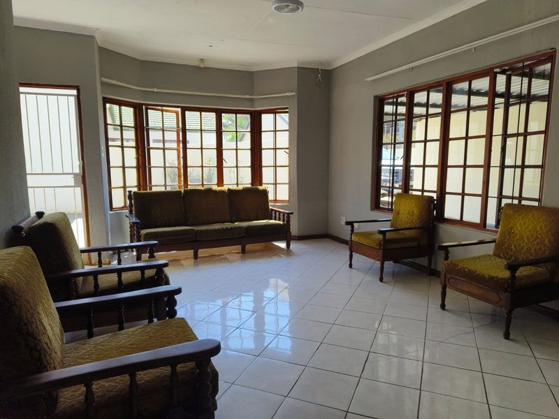 Spacious living room featuring large bay windows with wooden frames, tiled flooring, and a coved ceiling, offering a bright and functional living space.