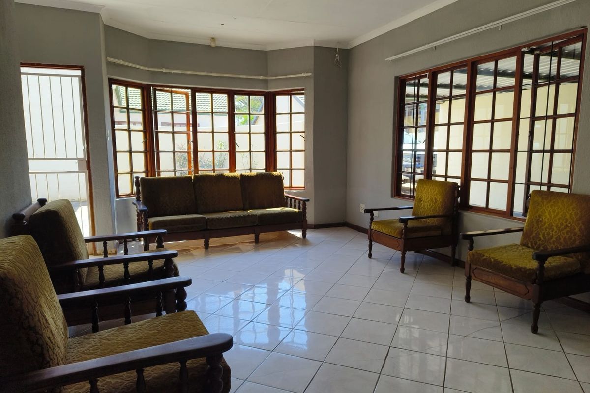 Spacious living room featuring large bay windows with wooden frames, tiled flooring, and a coved ceiling, offering a bright and functional living space.