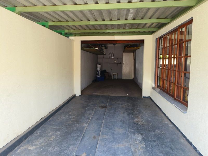 A covered garage space featuring concrete flooring, a corrugated metal roof, and a timber-framed window overlooking the interior area.