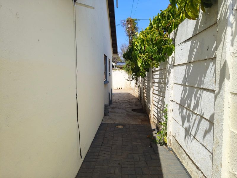 A narrow side passage of the townhouse featuring paved flooring and a concrete boundary wall with climbing vegetation.