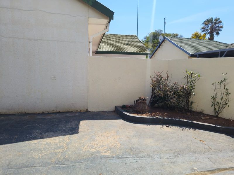 A rear exterior area featuring concrete paving, a boundary wall, and a raised garden bed, showing signs of wear and requiring maintenance.