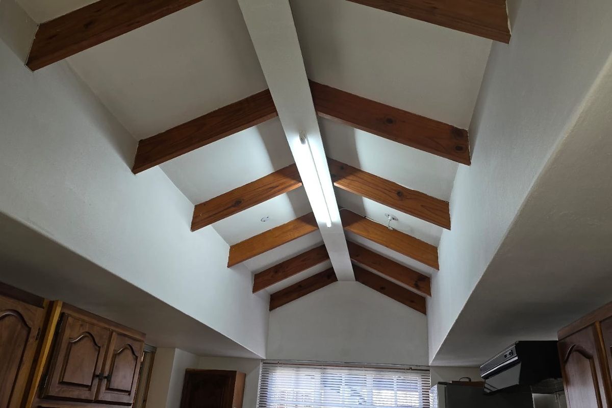 Kitchen area featuring a high vaulted ceiling with exposed timber beams, traditional timber cabinetry, and an integrated extractor fan.