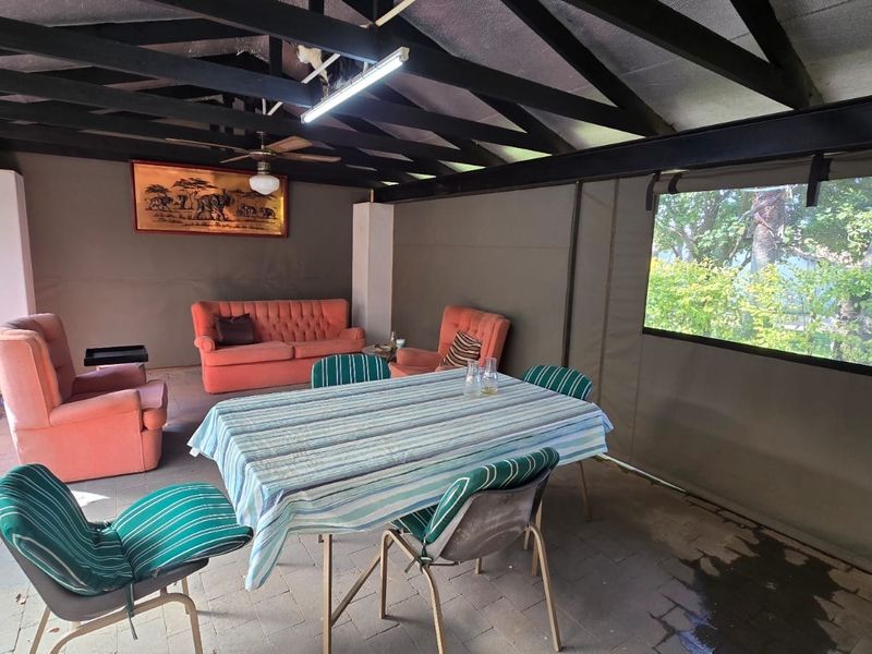 A covered outdoor patio area featuring exposed timber rafters, paved flooring, and retractable canvas side screens, providing a versatile space for outdoor living.