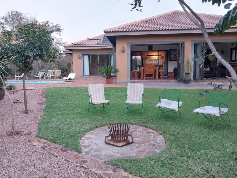 Rear view of the house featuring a landscaped garden, stone fire pit, swimming pool, and a covered patio with folding glass doors.
