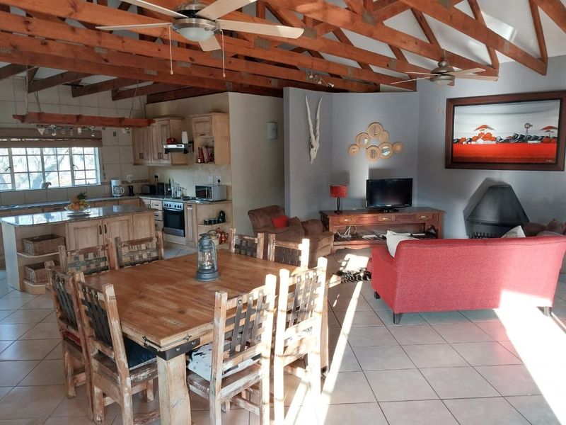 Spacious open-plan living, dining, and kitchen area featuring exposed timber roof trusses, tiled flooring, a central kitchen island, and a cozy fireplace.