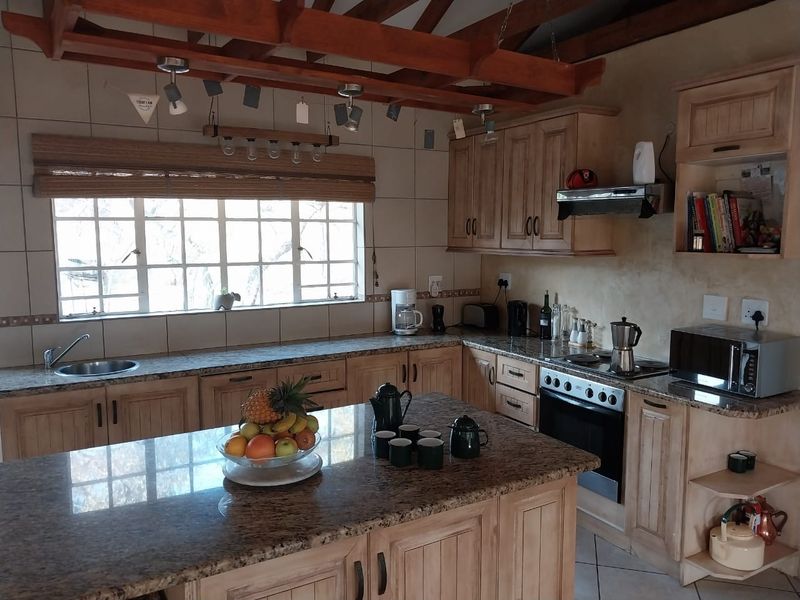 A rustic-style kitchen featuring wooden cabinetry, granite countertops, a central island, and exposed timber ceiling beams with a tiled backsplash.