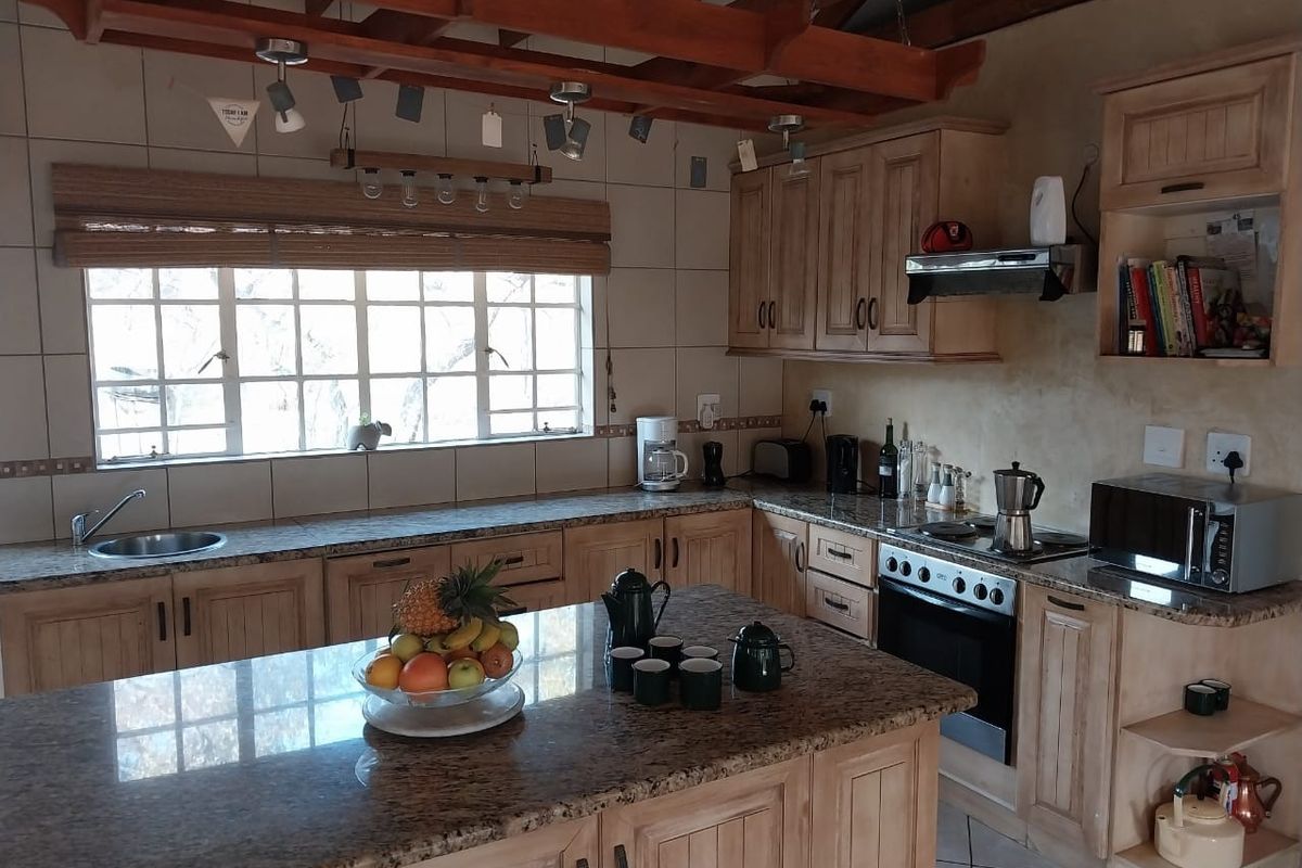 A rustic-style kitchen featuring wooden cabinetry, granite countertops, a central island, and exposed timber ceiling beams with a tiled backsplash.