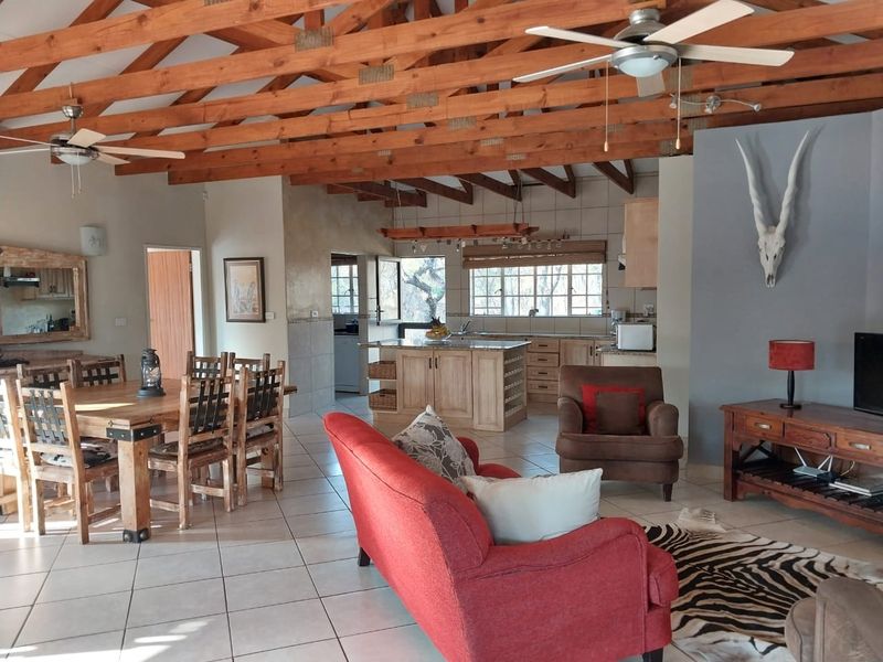 Spacious open-plan living and dining area featuring exposed timber roof trusses, tiled flooring, and a functional kitchen with a central island.