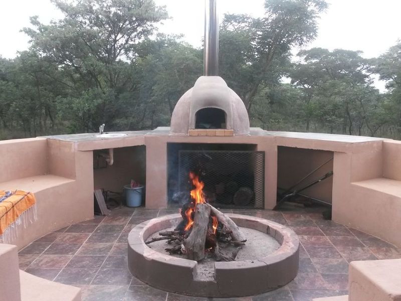 Outdoor entertainment area featuring a built-in pizza oven, braai, integrated sink, and circular fire pit with built-in bench seating.