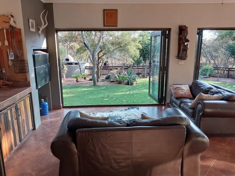 Open-plan living area featuring tiled floors, a built-in braai, and large bi-fold doors opening onto a landscaped garden.