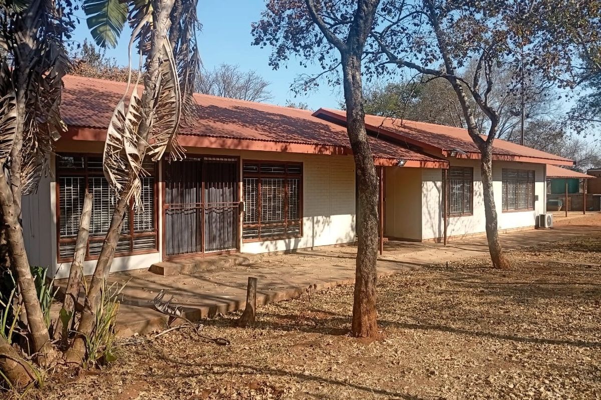 Rear view of the property featuring a paved patio area, corrugated metal roofing, and large windows with security gates.