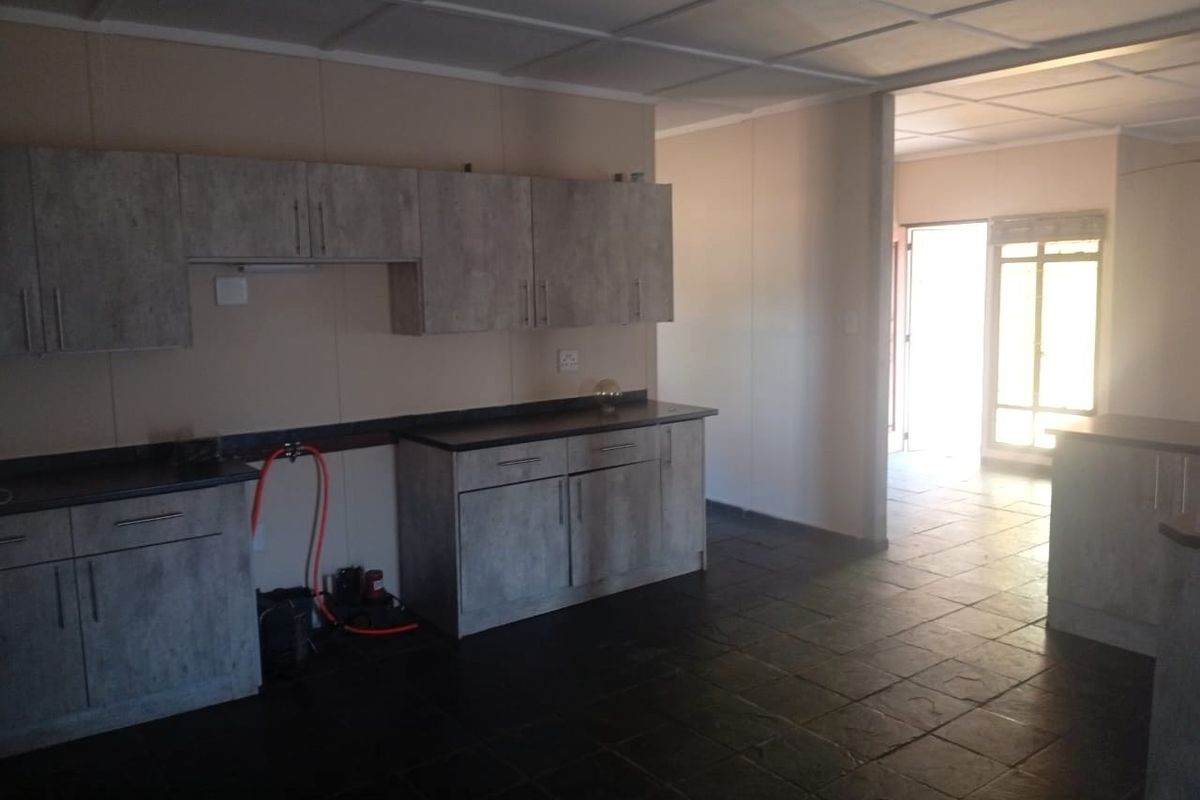 An empty kitchen area featuring modern grey-toned cabinetry, dark tiled flooring, and a drop ceiling, leading into an adjacent living space.
