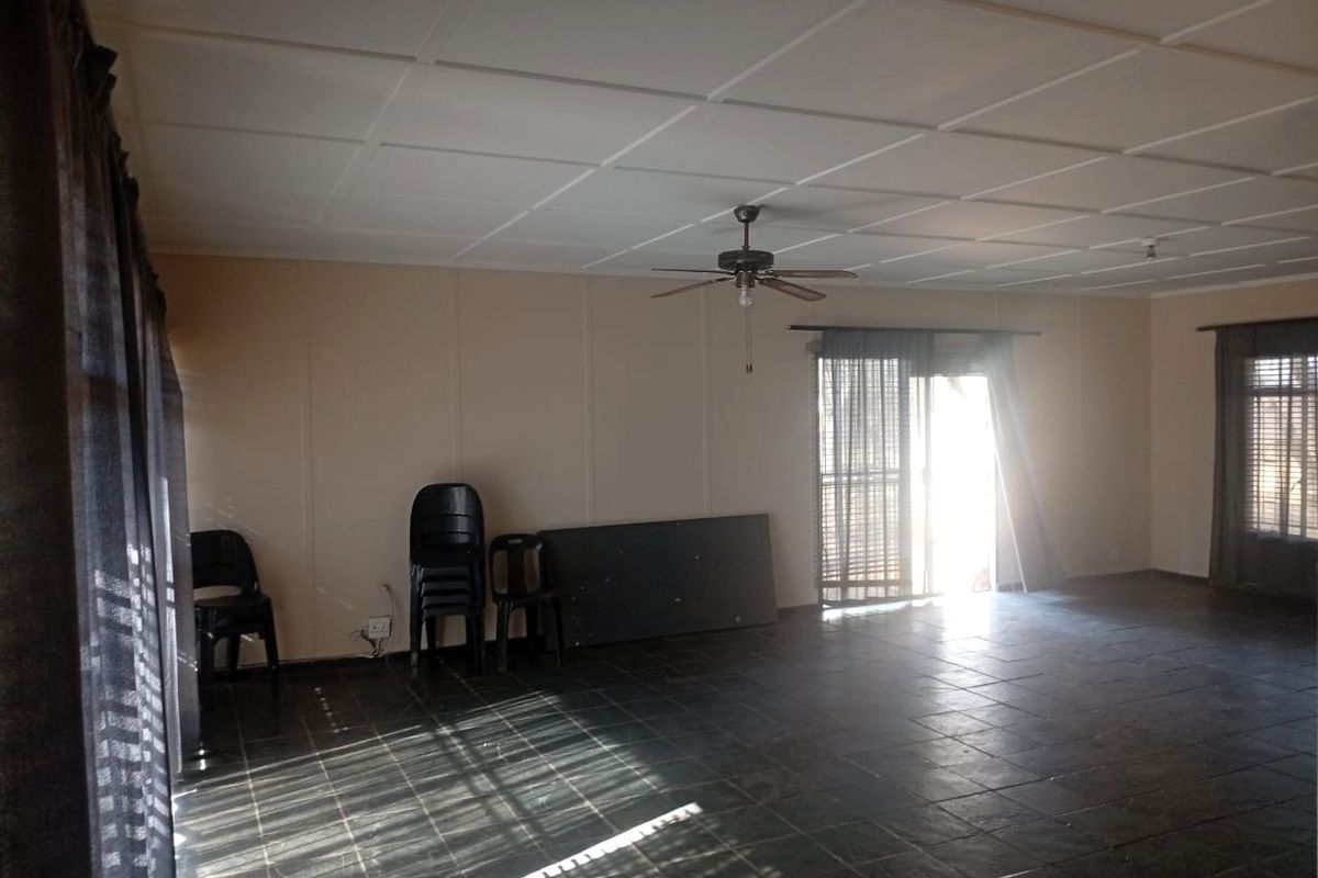 Spacious living area featuring dark tiled flooring, a ceiling fan, and large sliding glass doors providing natural light.