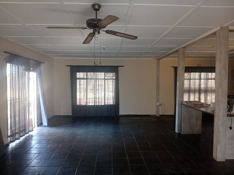 Spacious open-plan living area featuring dark tiled flooring, a ceiling fan, and a breakfast bar, offering a versatile layout with natural light.