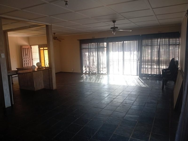 Spacious open-plan living area featuring dark tiled flooring, ceiling fans, and large sliding glass doors providing natural light and access to the exterior.