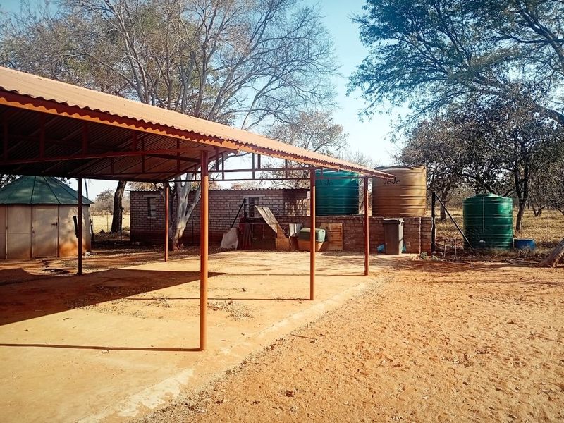 Outdoor area featuring a covered steel-framed structure, concrete slab, and multiple water storage tanks on a small holding property.