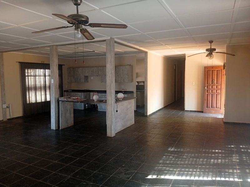 Spacious open-plan living and kitchen area featuring dark tiled flooring, a central kitchen island, and dual ceiling fans in a neutral setting.