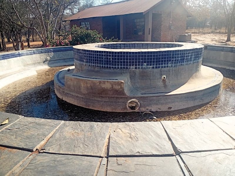 Outdoor pool area featuring a raised circular water feature with stone paving and an adjacent brick building, currently requiring maintenance and refurbishment.