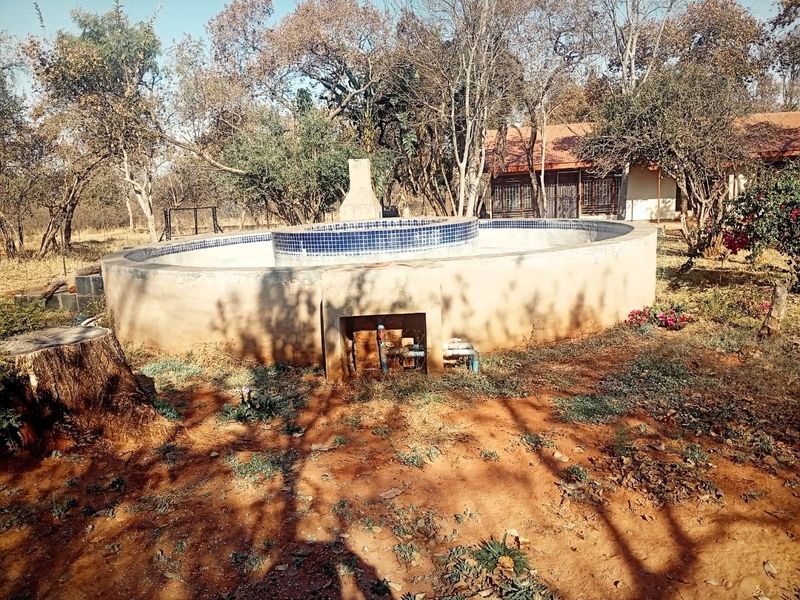 An outdoor circular swimming pool structure featuring tiled coping and exposed plumbing, situated in a natural garden setting requiring completion and landscaping.
