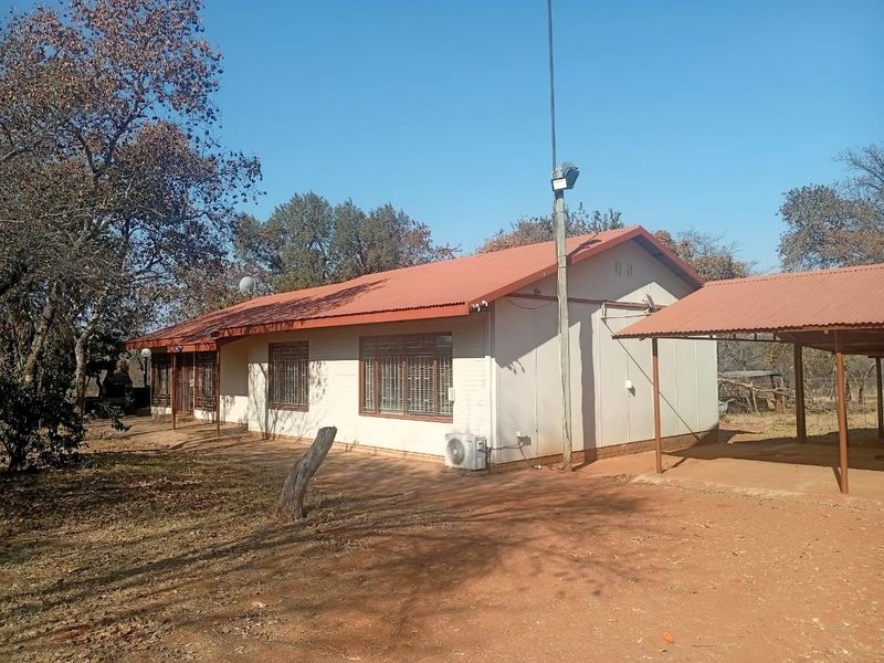 Front view of a single-story small holding property featuring a corrugated metal roof, security bars on windows, and an attached carport.