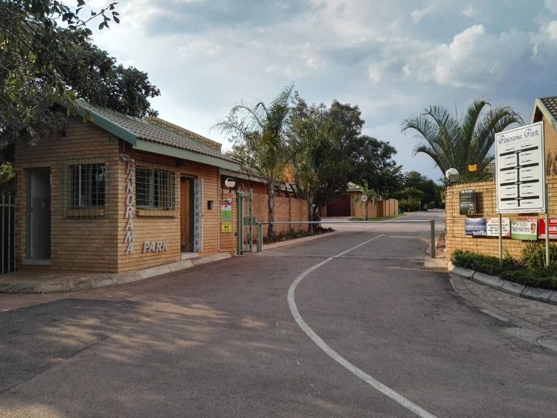 Entrance view of Panorama Park residential estate featuring a brick security gatehouse, boom gate access control, and paved road infrastructure.