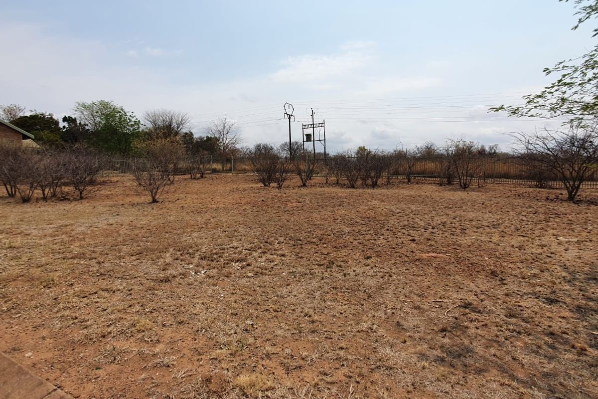 A vacant residential plot featuring dry, undeveloped land enclosed by perimeter fencing with overhead power lines visible in the background.