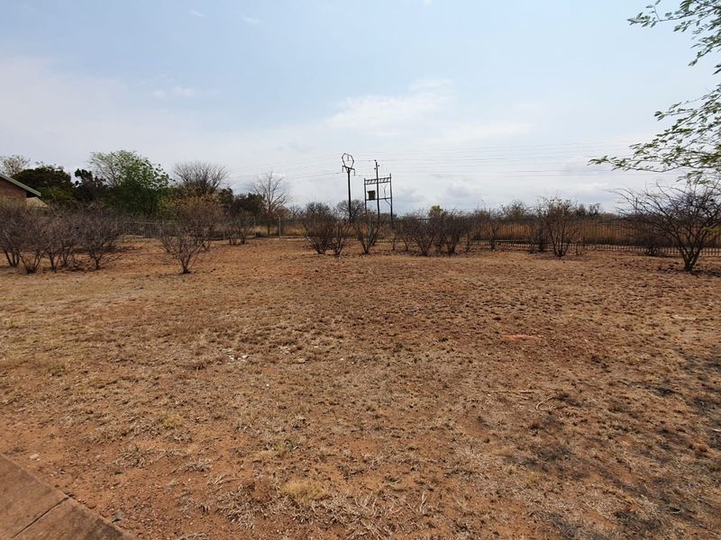A vacant residential plot featuring dry, undeveloped land enclosed by perimeter fencing with overhead power lines visible in the background.