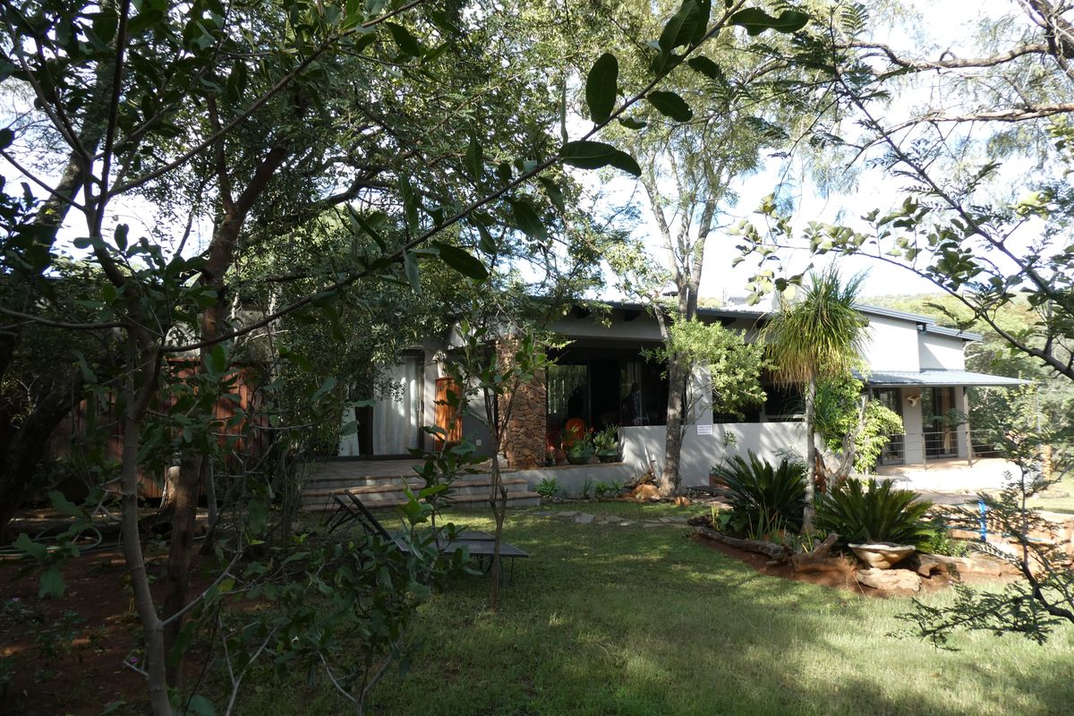 A view of the rear elevation featuring a covered patio, stone accents, and a well-established garden setting.