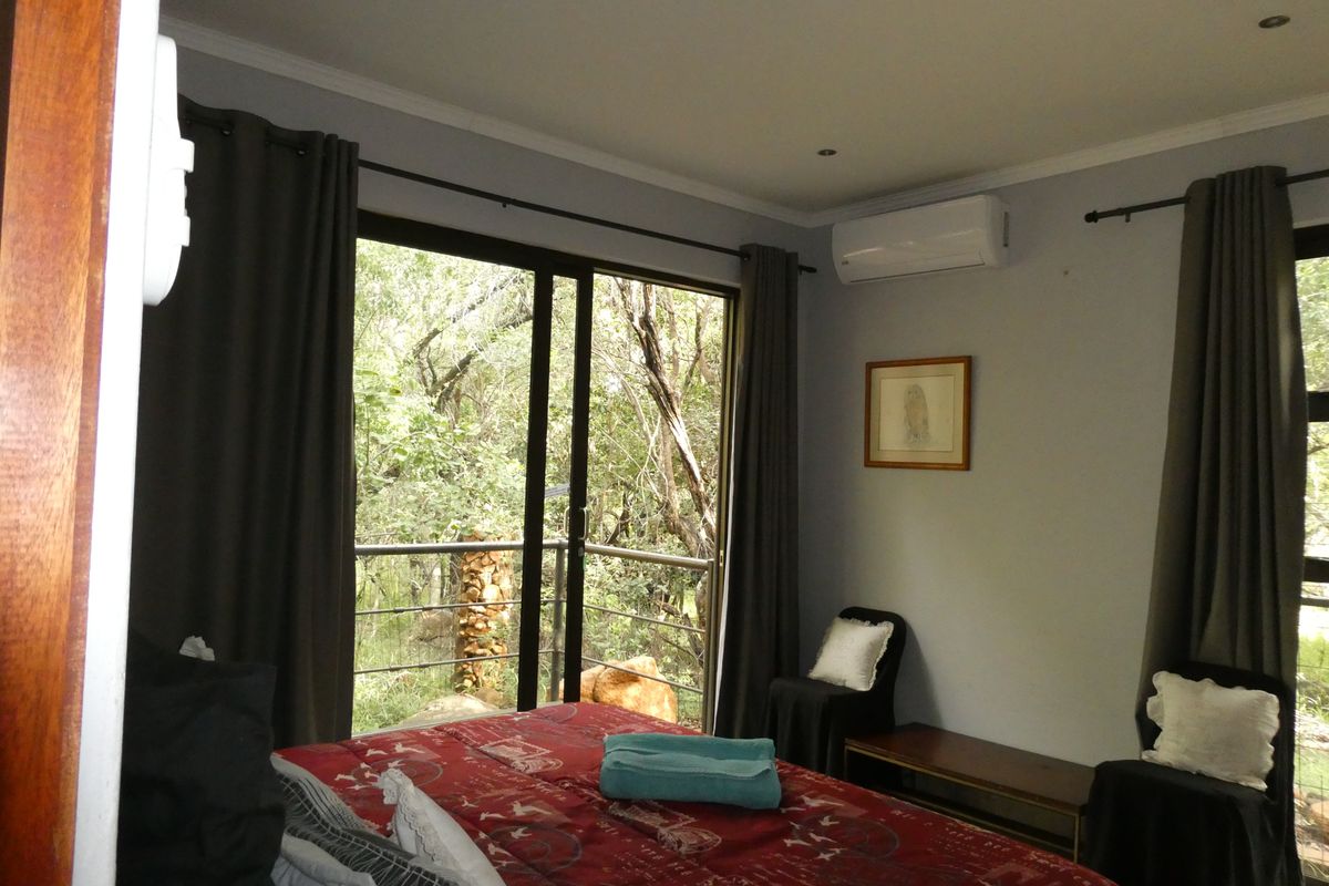 A well-lit bedroom featuring sliding glass doors that open to a balcony with natural views, equipped with a split-system air conditioner.