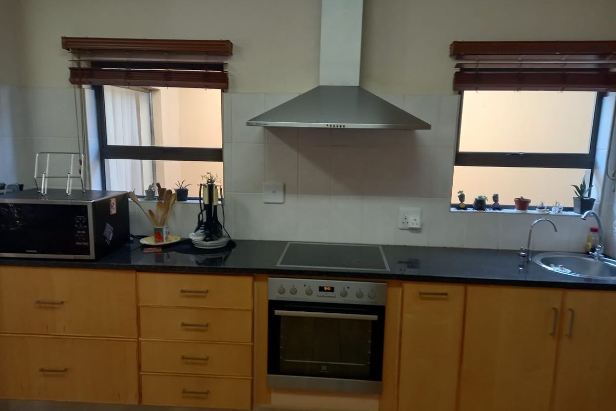 A functional kitchen featuring light wood cabinetry, dark granite countertops, a built-in oven, electric hob, and stainless steel extractor fan.
