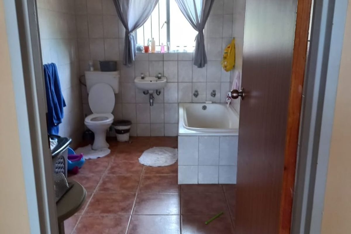 A functional bathroom featuring a bathtub, wall-mounted basin, and toilet with tiled walls and flooring.