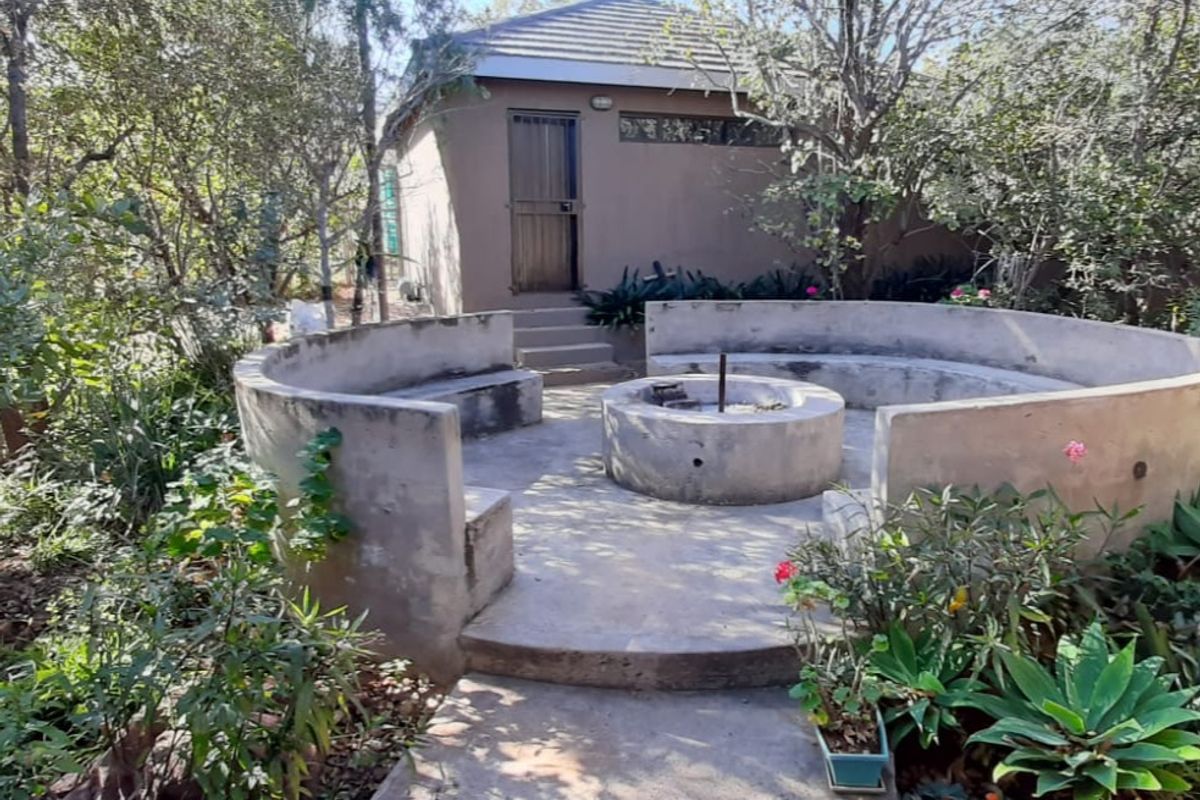 Outdoor entertainment area featuring a built-in concrete fire pit and circular seating, set within a garden space adjacent to a small outbuilding.