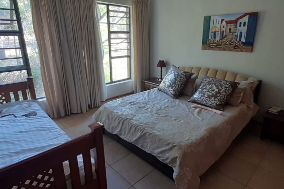 A functional bedroom featuring tiled flooring and large windows with security bars, providing natural light and a view of the exterior.