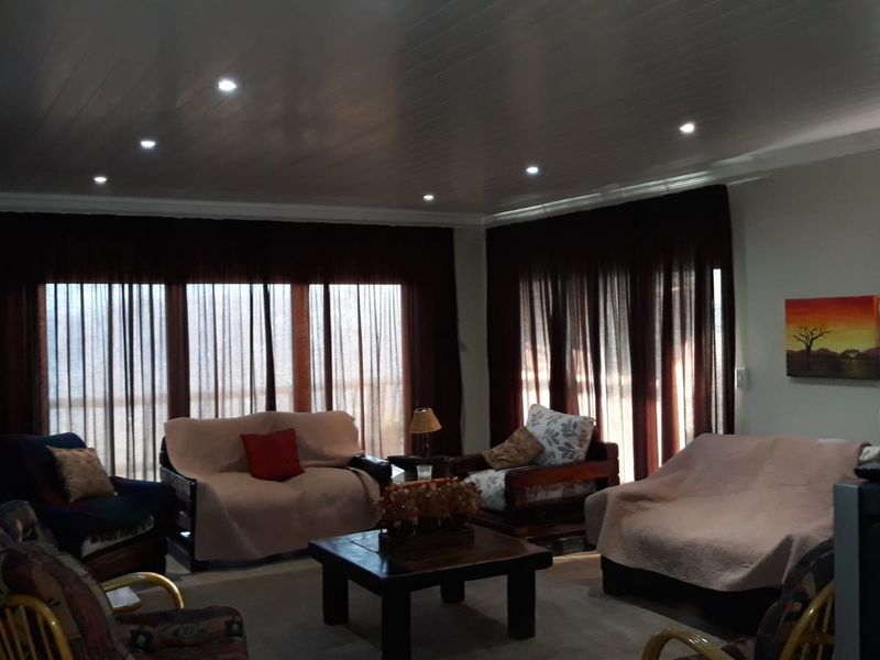 A spacious living room featuring a tongue and groove ceiling with recessed downlighting and large windows covered by dark curtains.