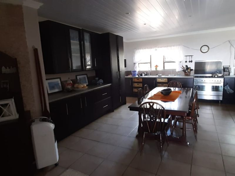 Spacious open-plan kitchen and dining area featuring dark cabinetry, stainless steel appliances, tiled flooring, and a classic tongue and groove ceiling.