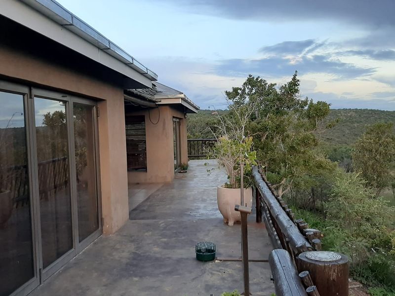 A spacious outdoor patio featuring concrete flooring, log railings, and large sliding glass doors, offering scenic views of the surrounding natural landscape.
