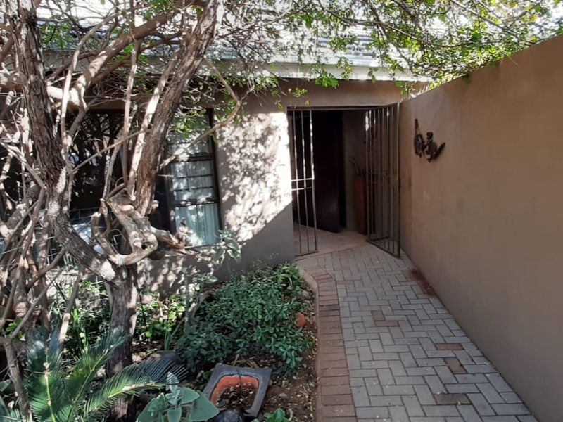 A paved walkway leads to the front entrance of the house, featuring a security gate and established garden area.
