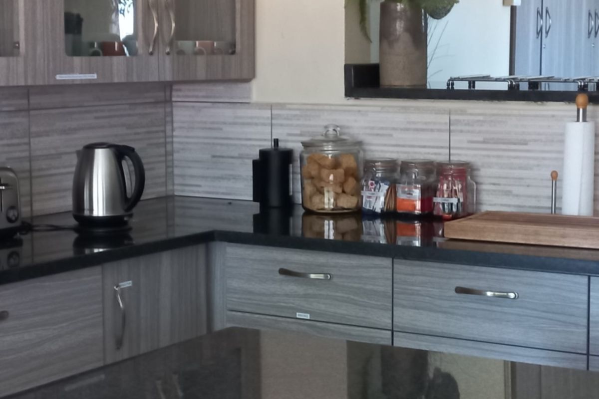A functional kitchen area featuring dark granite countertops, grey wood-grain cabinetry, and a tiled backsplash.